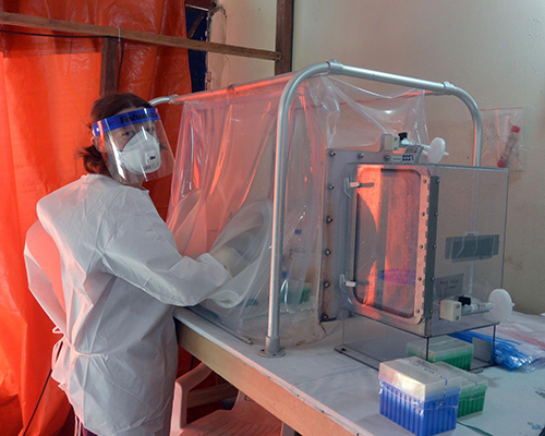 One of the NIAID study authors is shown at the diagnostic laboratory in Monrovia using a sealed glovebox to inactivate virus in patient blood samples prior to testing for Ebola. [NIAID]