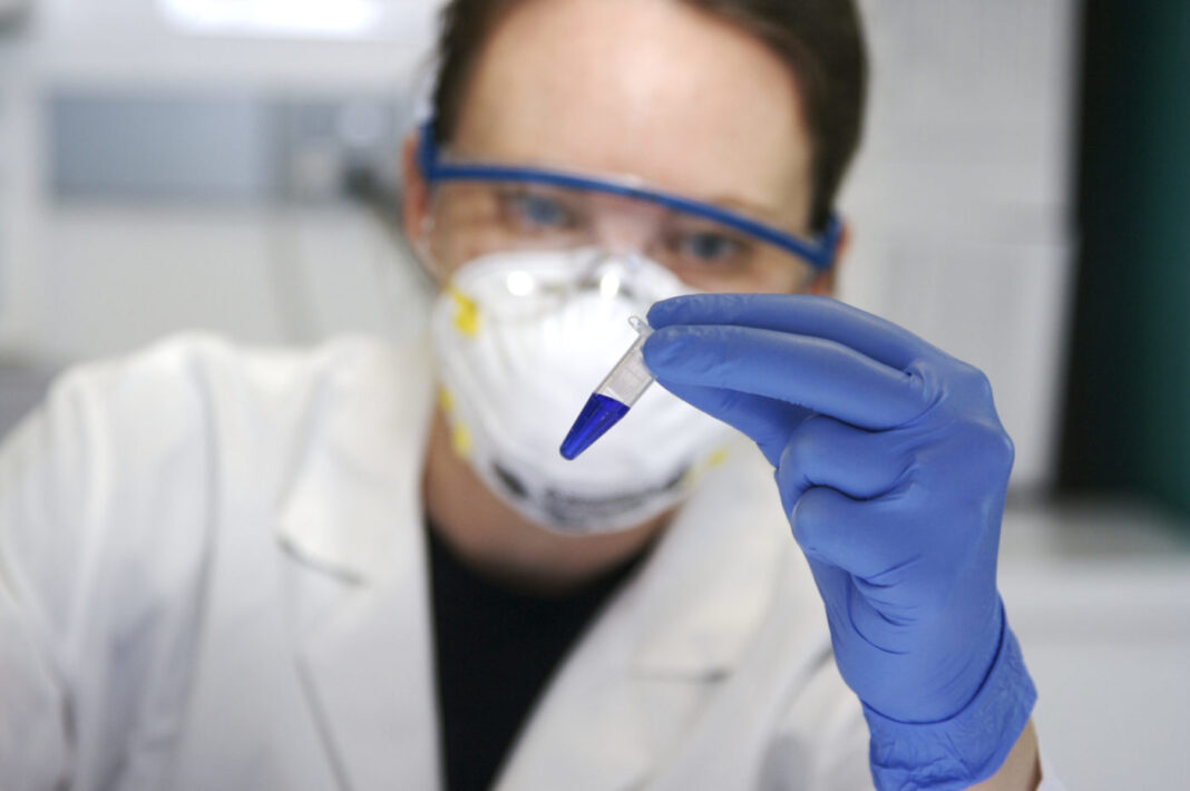 Female scientist looks at tube with blue liquid