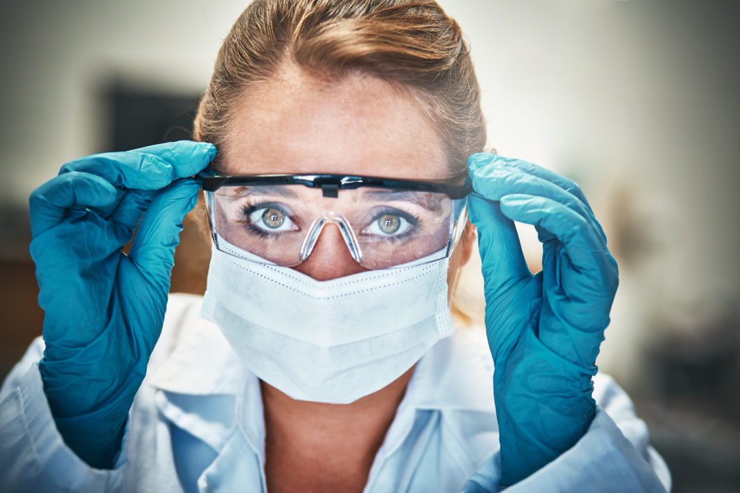 Woman scientist adjusts protective goggles, staring intently