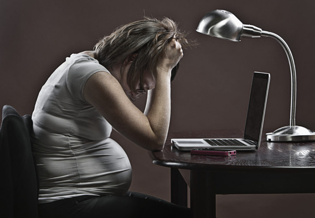 Stressed pregnant business woman sitting at desk in front of laptop