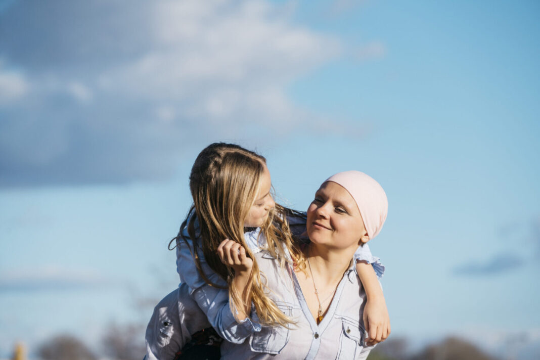 A woman with cancer is next to her daughter. A girl is hugging a woman happy