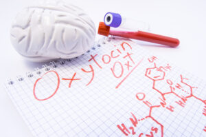 Note inscribed with hormone Oxytocin and chemical formula lies surrounded by 3d brain and lab test tubes with blood for analysis. Diagnosis levels of oxytocin, its use in medicine and effects on body