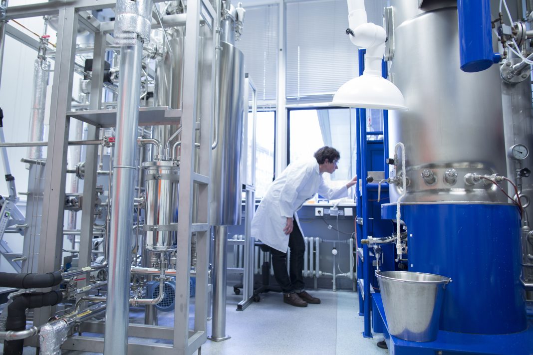 Woman with lab coat in technical room with a fermenter