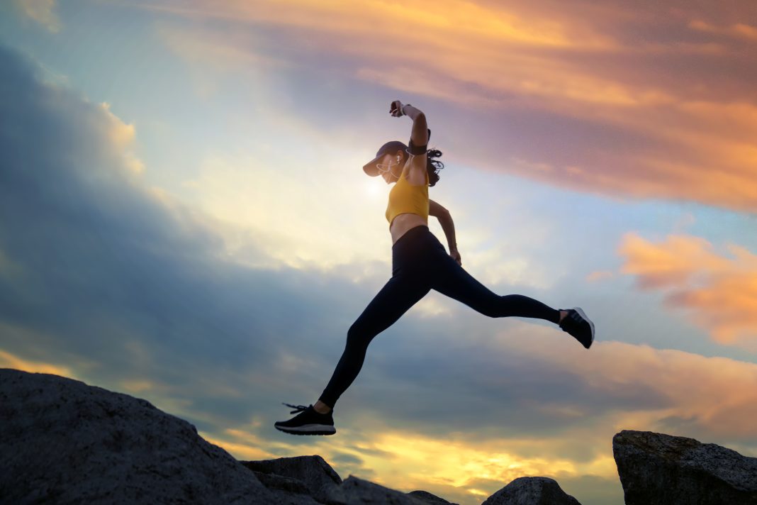 Asian woman runs and jumping on mountain ridge at sunset.