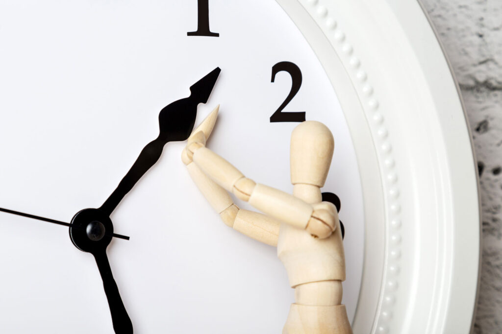 Wooden human figure trying to stop the arrow of the clock. Aging concept