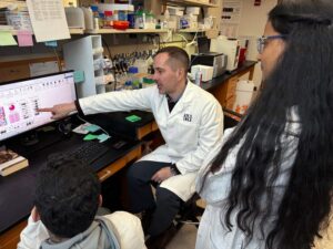 Corresponding study author Jeffrey Savas points at a computer as he and his lab members discuss their recent paper in Science Translational Medicine. [Northwestern University]