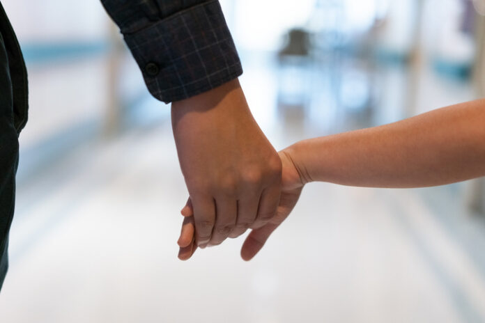 Cropped image of father holding daughter's hand. Man and girl are walking together. They are in hospital corridor.